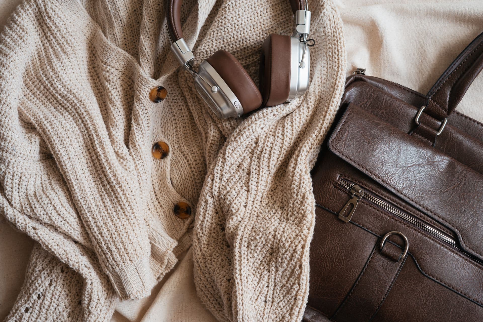 A soft cream knit, leather bag and accessories laid together in neutral tones