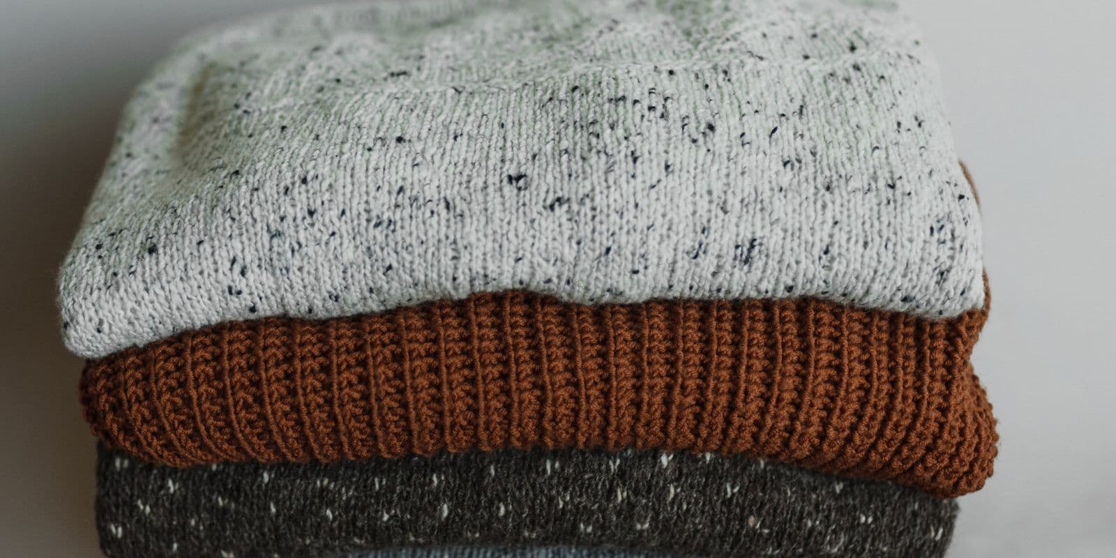 A folded stack of knit sweaters in grey and charcoal