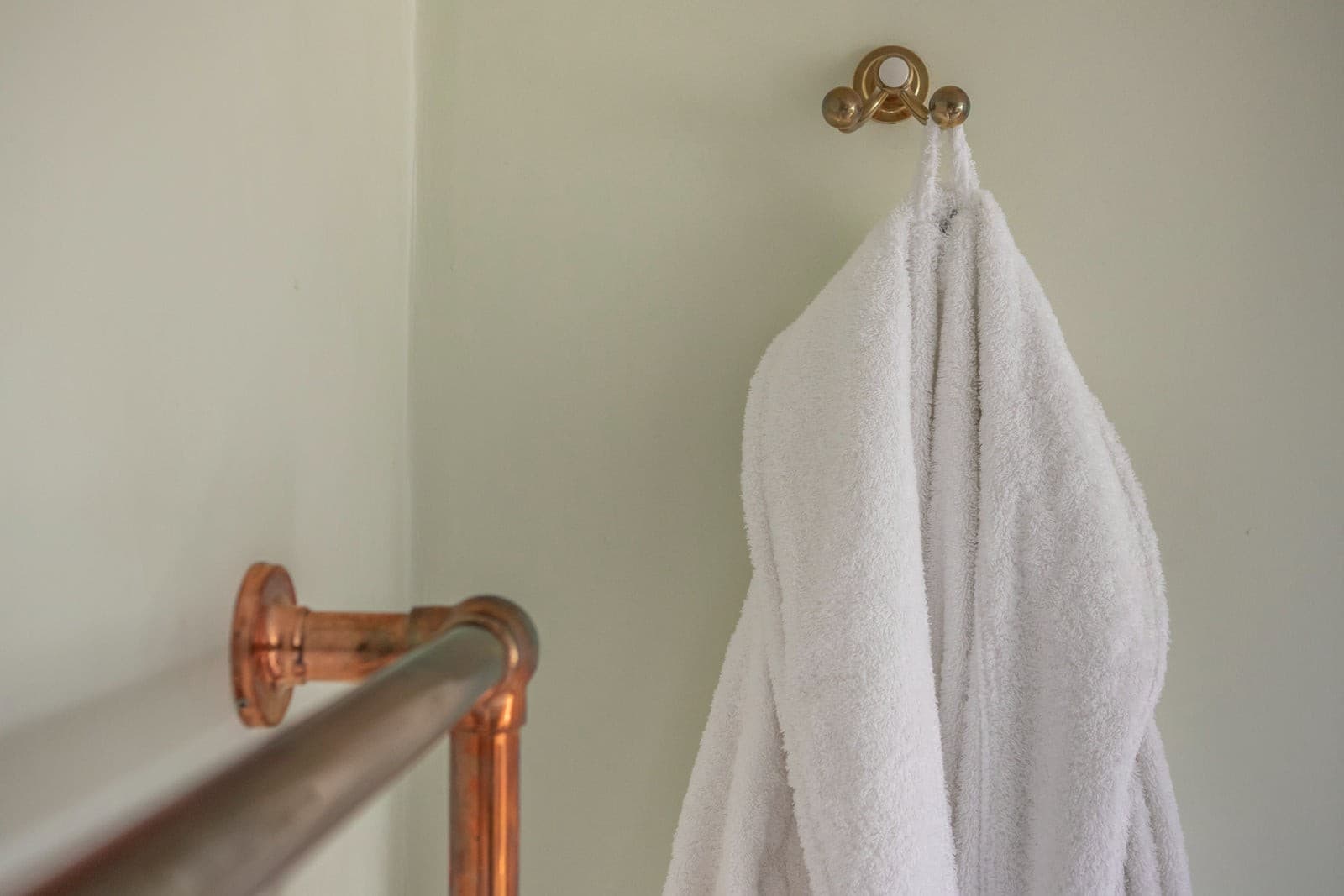 White cotton towelling robe hung on a brass hook