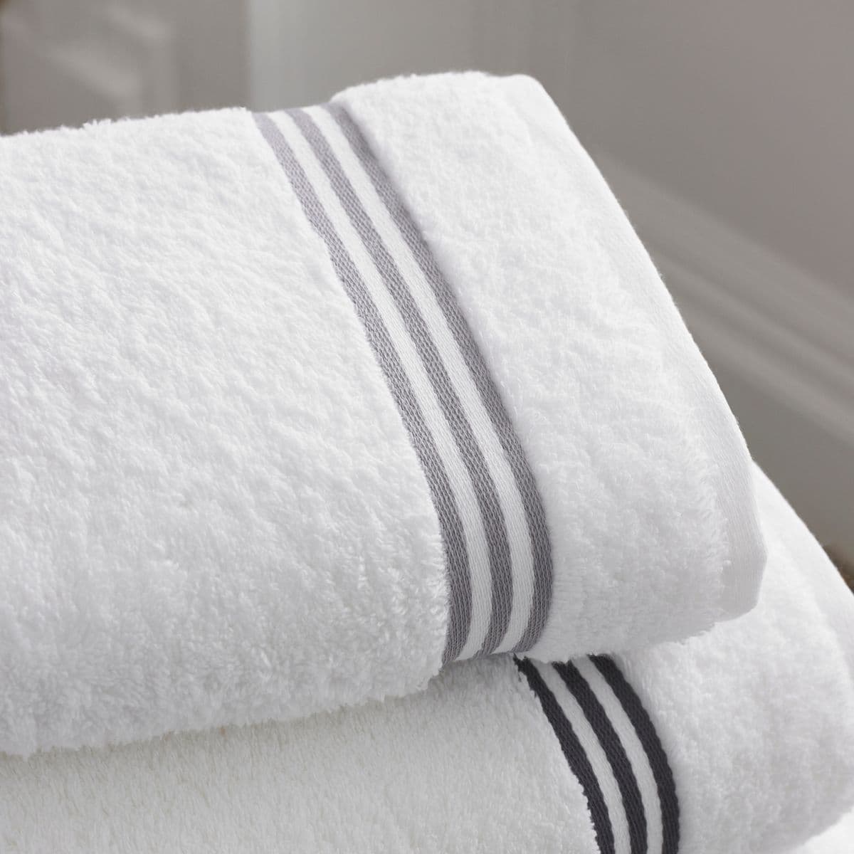 Two crisp white bath towels with a subtle grey border, neatly folded